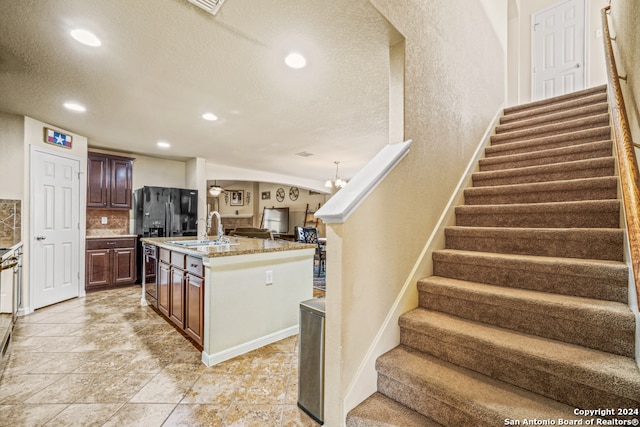 kitchen with decorative backsplash, a center island with sink, a textured ceiling, a notable chandelier, and sink