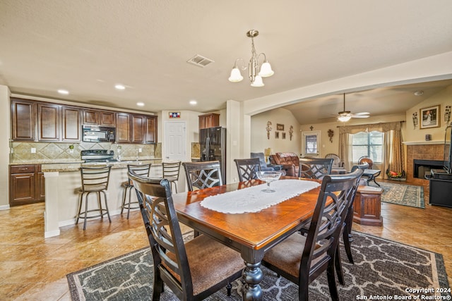 dining space with lofted ceiling, a tile fireplace, and ceiling fan with notable chandelier