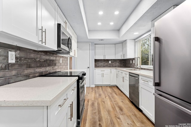 kitchen with appliances with stainless steel finishes, white cabinets, sink, and light wood-type flooring