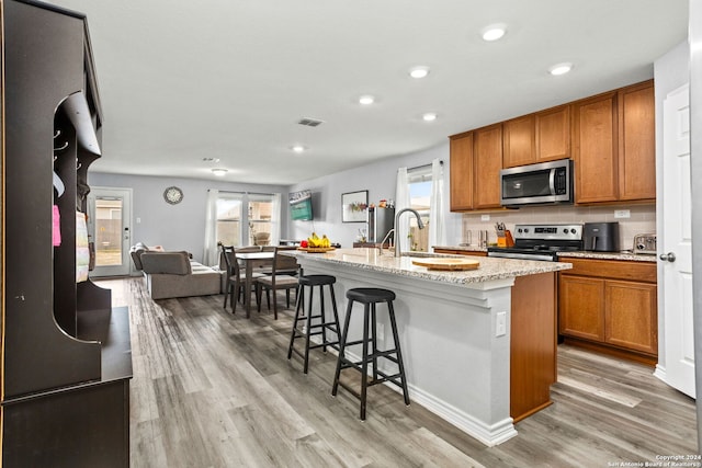 kitchen featuring a kitchen island with sink, light hardwood / wood-style flooring, stainless steel appliances, and plenty of natural light