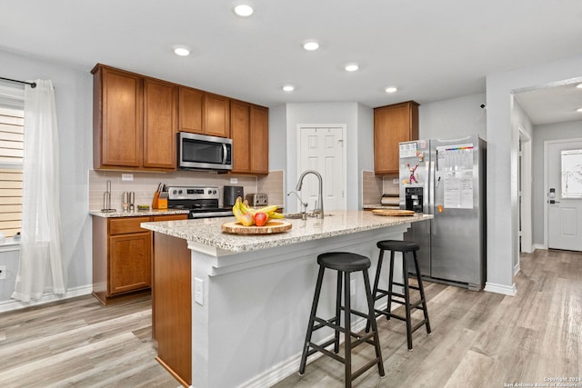 kitchen with appliances with stainless steel finishes, plenty of natural light, a kitchen island with sink, and light wood-type flooring