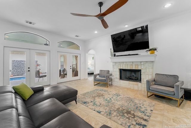 tiled living room with ornamental molding, french doors, ceiling fan, and a stone fireplace