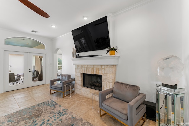 living room with a stone fireplace, french doors, ceiling fan, and crown molding