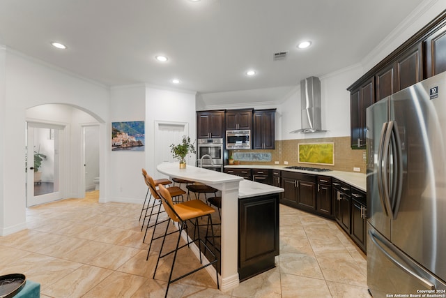 kitchen featuring appliances with stainless steel finishes, tasteful backsplash, a kitchen bar, wall chimney exhaust hood, and an island with sink