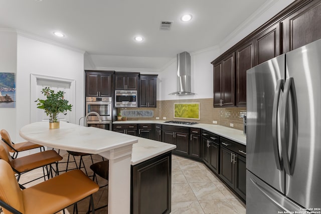 kitchen featuring ornamental molding, a center island with sink, stainless steel appliances, a kitchen bar, and wall chimney exhaust hood