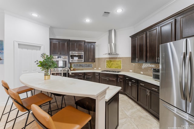 kitchen featuring a kitchen island with sink, wall chimney range hood, a breakfast bar, backsplash, and appliances with stainless steel finishes