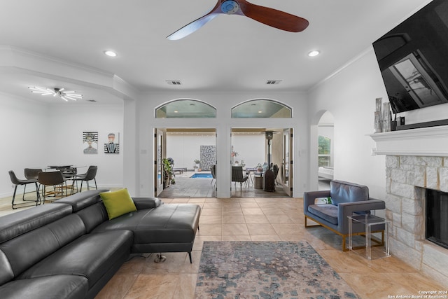 living room featuring a stone fireplace, light tile patterned floors, ceiling fan, and crown molding