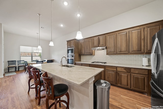 kitchen featuring an island with sink, stainless steel appliances, sink, decorative light fixtures, and light hardwood / wood-style floors