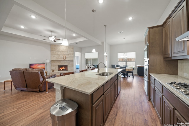 kitchen featuring a kitchen island with sink, wood-type flooring, sink, decorative light fixtures, and a fireplace