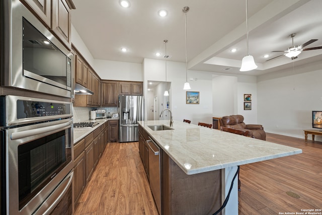 kitchen with a spacious island, wood-type flooring, stainless steel appliances, sink, and decorative light fixtures