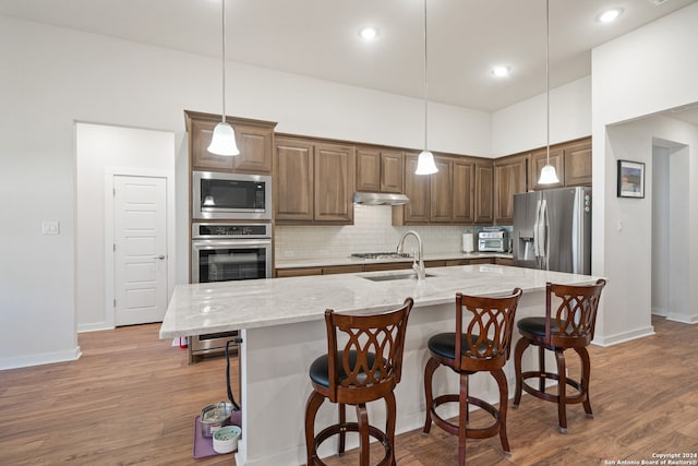 kitchen featuring appliances with stainless steel finishes, light stone countertops, hanging light fixtures, and an island with sink