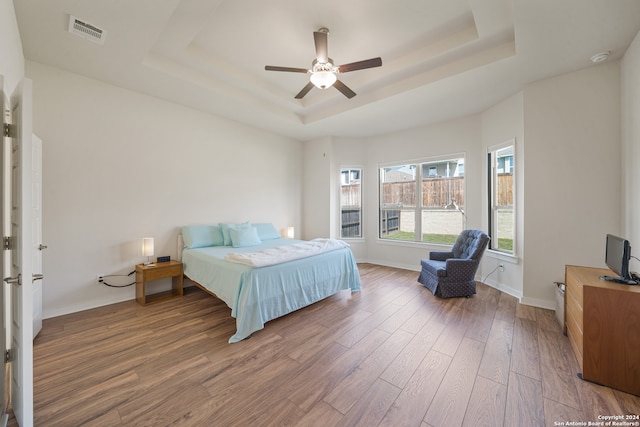 bedroom with ceiling fan, wood-type flooring, and a raised ceiling