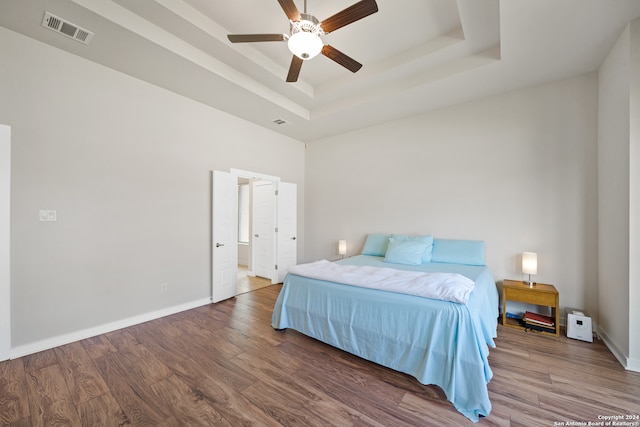 bedroom with hardwood / wood-style flooring, a tray ceiling, and ceiling fan