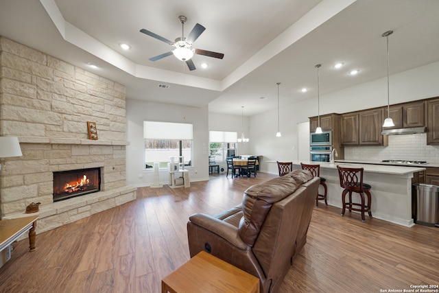 living room with light hardwood / wood-style flooring, a fireplace, ceiling fan with notable chandelier, and a raised ceiling