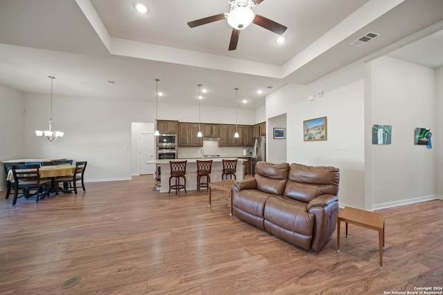 living room featuring a tray ceiling, dark hardwood / wood-style floors, and ceiling fan with notable chandelier