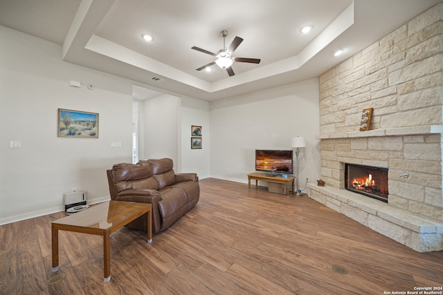 living room featuring ceiling fan, a raised ceiling, a stone fireplace, and hardwood / wood-style floors