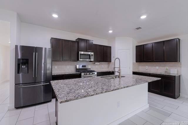 kitchen with a kitchen island with sink, dark brown cabinets, backsplash, sink, and appliances with stainless steel finishes