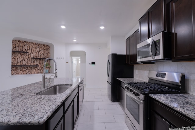 kitchen with sink, appliances with stainless steel finishes, light stone counters, and an island with sink