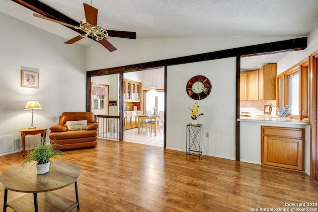 living room featuring light hardwood / wood-style flooring, vaulted ceiling with beams, a textured ceiling, and a healthy amount of sunlight