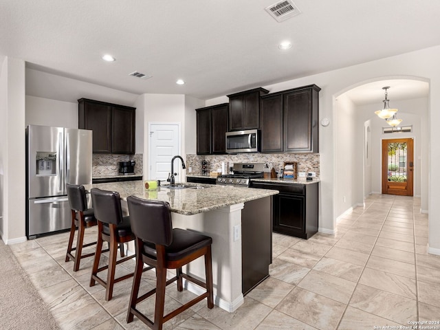 kitchen with backsplash, an island with sink, stainless steel appliances, sink, and light stone counters