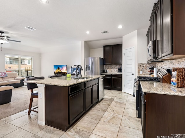 kitchen with light stone countertops, sink, an island with sink, backsplash, and stainless steel appliances