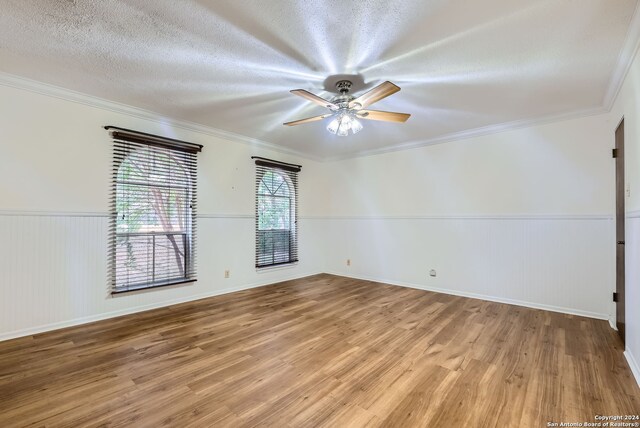 empty room featuring wood walls, a textured ceiling, hardwood / wood-style floors, ceiling fan, and ornamental molding