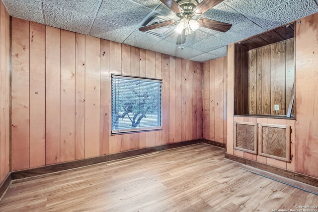 empty room with light hardwood / wood-style floors, a drop ceiling, wooden walls, and ceiling fan