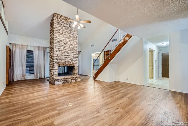 unfurnished living room featuring light hardwood / wood-style floors, a stone fireplace, a textured ceiling, high vaulted ceiling, and ceiling fan