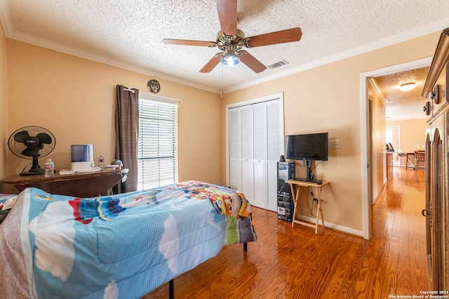 bedroom with a textured ceiling, ceiling fan, crown molding, wood-type flooring, and a closet