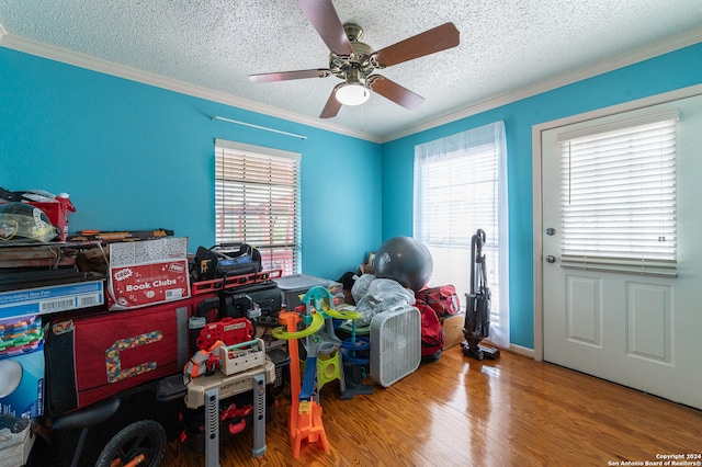 recreation room with ceiling fan, wood-type flooring, a textured ceiling, and ornamental molding