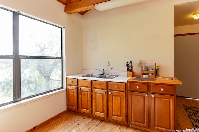 kitchen with beamed ceiling, light wood-type flooring, and sink