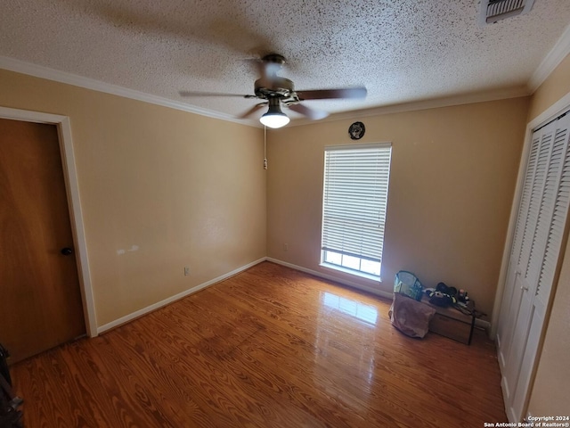 unfurnished bedroom featuring wood-type flooring, a textured ceiling, ceiling fan, and ornamental molding