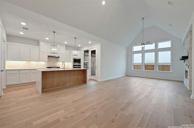 kitchen featuring tasteful backsplash, hanging light fixtures, a large island, ceiling fan with notable chandelier, and white cabinets