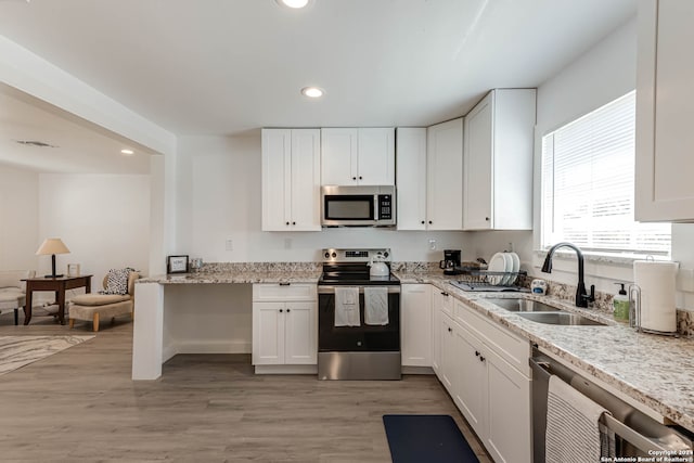 kitchen with white cabinets, appliances with stainless steel finishes, light stone countertops, light hardwood / wood-style flooring, and sink