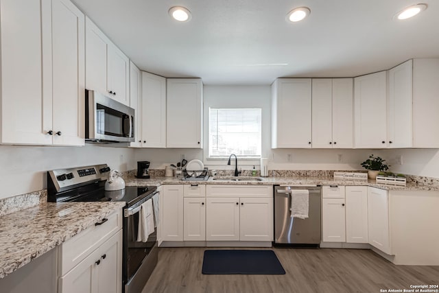 kitchen with appliances with stainless steel finishes, sink, light hardwood / wood-style floors, white cabinets, and light stone counters