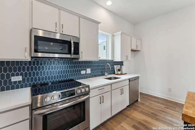 kitchen with decorative backsplash, light hardwood / wood-style flooring, stainless steel appliances, sink, and white cabinets