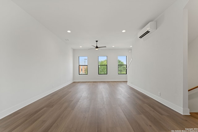 unfurnished room with a wall unit AC, hardwood / wood-style flooring, and ceiling fan