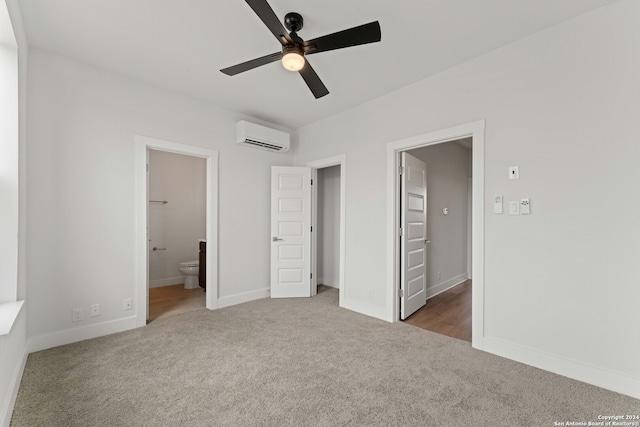 unfurnished bedroom featuring a closet, an AC wall unit, dark carpet, a walk in closet, and ensuite bath