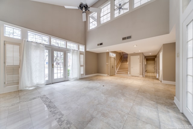 unfurnished living room with a towering ceiling, a healthy amount of sunlight, and ceiling fan