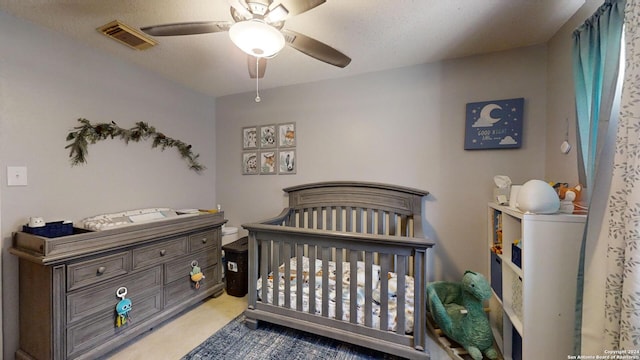 carpeted bedroom featuring a textured ceiling, a crib, and ceiling fan