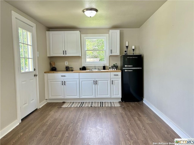 kitchen with sink, hardwood / wood-style floors, white cabinets, and black fridge