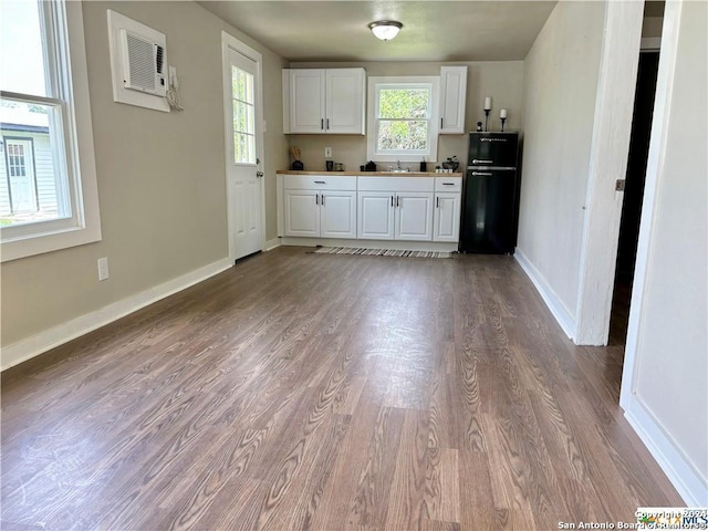 kitchen with white cabinets, black fridge, hardwood / wood-style flooring, an AC wall unit, and sink