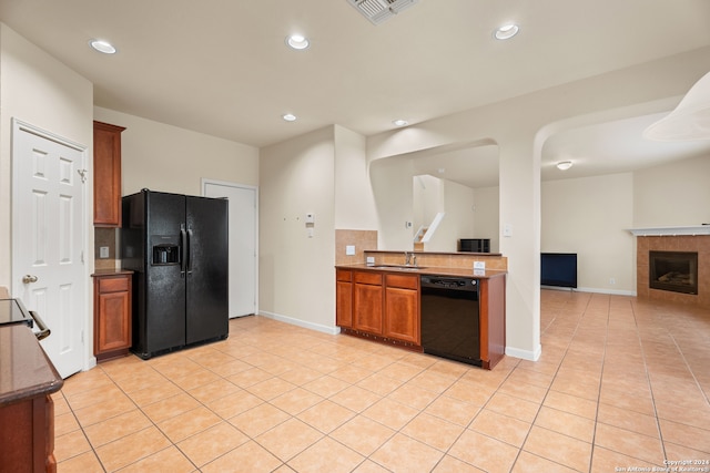 kitchen featuring a tiled fireplace, backsplash, light tile patterned floors, black appliances, and sink