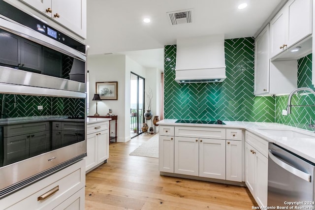 kitchen featuring light wood-type flooring, premium range hood, stainless steel appliances, sink, and white cabinets