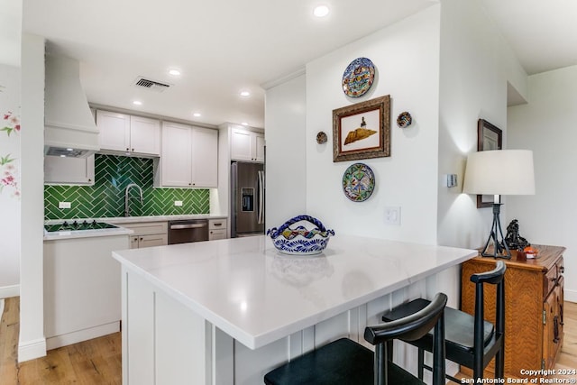 kitchen featuring a breakfast bar, premium range hood, white cabinets, kitchen peninsula, and stainless steel appliances