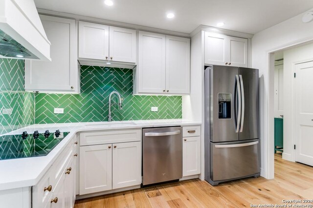 kitchen with white cabinetry, sink, light hardwood / wood-style floors, exhaust hood, and appliances with stainless steel finishes