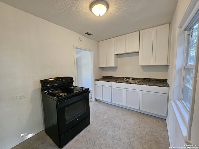 kitchen featuring visible vents, black range with electric stovetop, a sink, dark countertops, and white cabinets