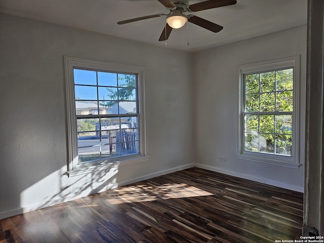 empty room featuring dark wood-type flooring, a ceiling fan, and baseboards