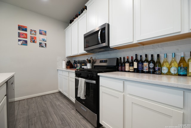 kitchen with stainless steel appliances, backsplash, light stone countertops, white cabinets, and light hardwood / wood-style floors