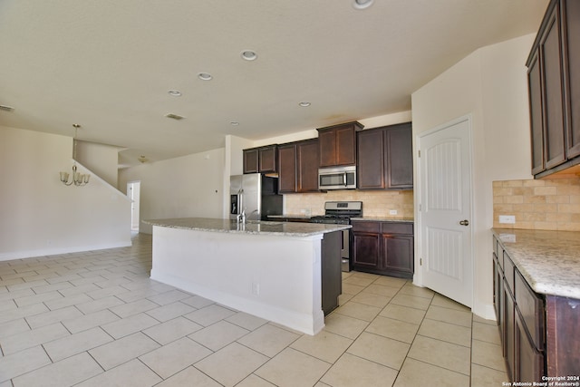 kitchen featuring tasteful backsplash, a center island with sink, light stone counters, dark brown cabinetry, and stainless steel appliances